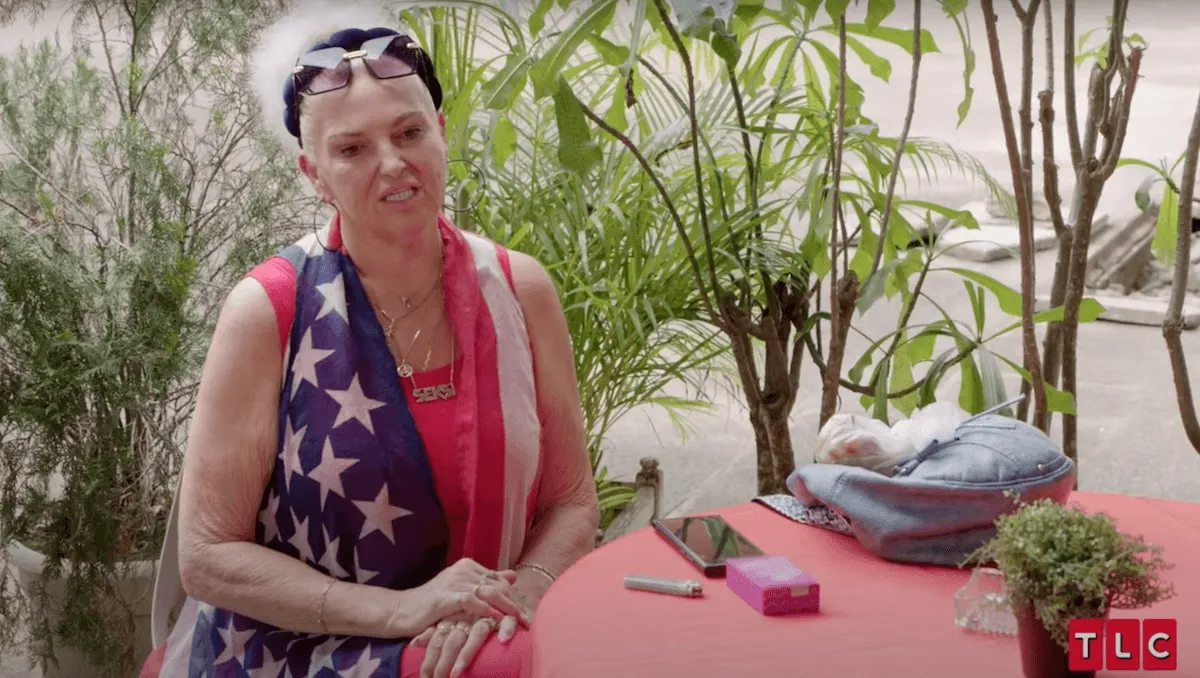 Angela Deem sitting at a table wearing an American flag outfit in '90 Day Fiance: Happily Ever After?' Season 8