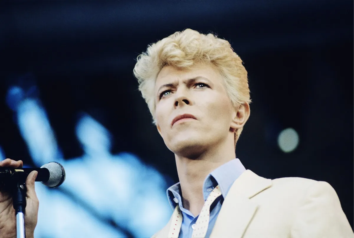 David Bowie performing The Serious Moonlight show in Vancouver, Canada in a white blazer and blue collared shirt.