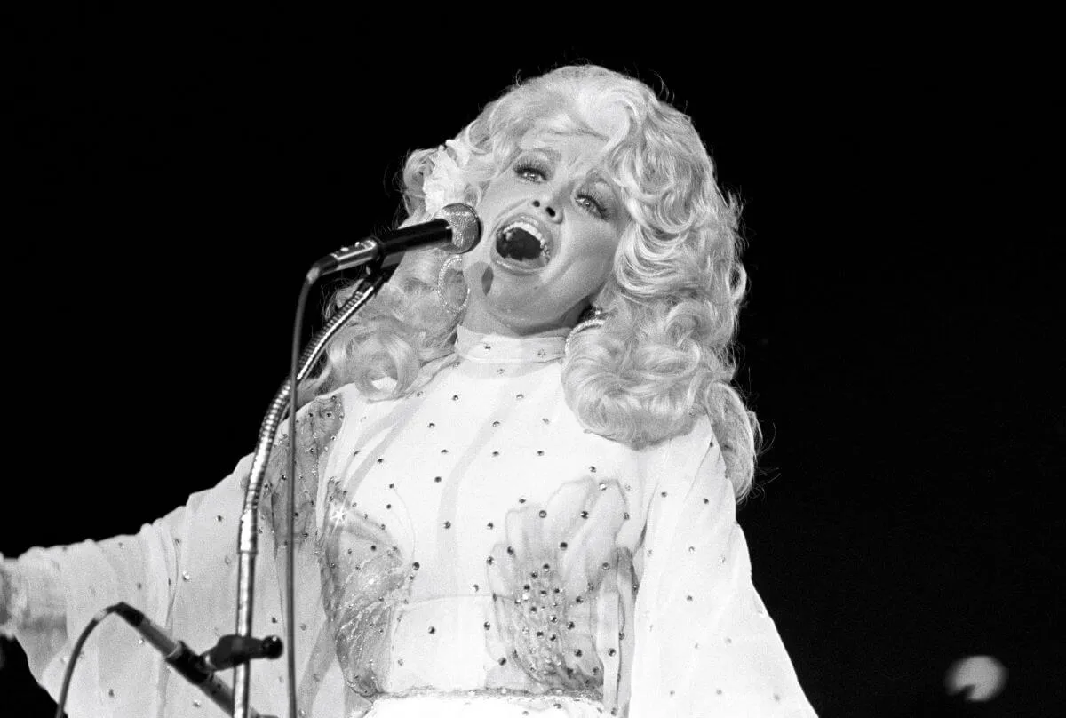 A black and white picture of Dolly Parton singing into a microphone.