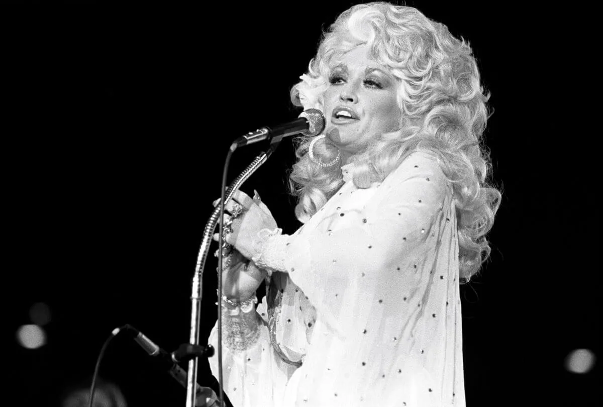 A black and white picture of Dolly Parton standing in front of a microphone.