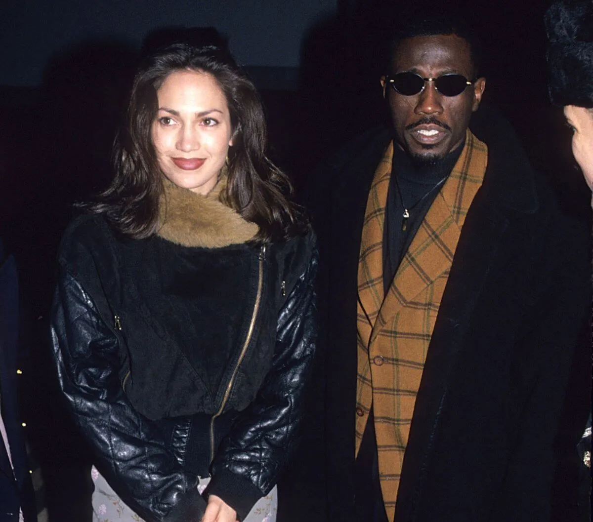 Jennifer Lopez and Wesley Snipes walk together. They both wear coats and he wears sunglasses.