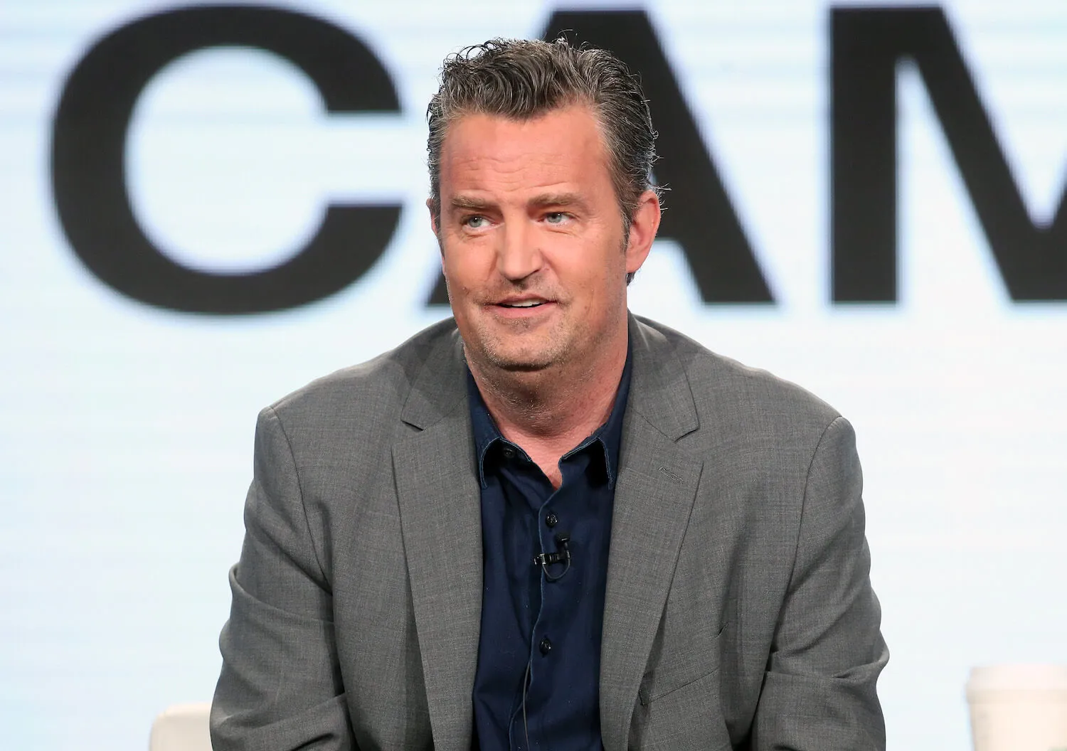 Matthew Perry in a gray suit speaking in 2017