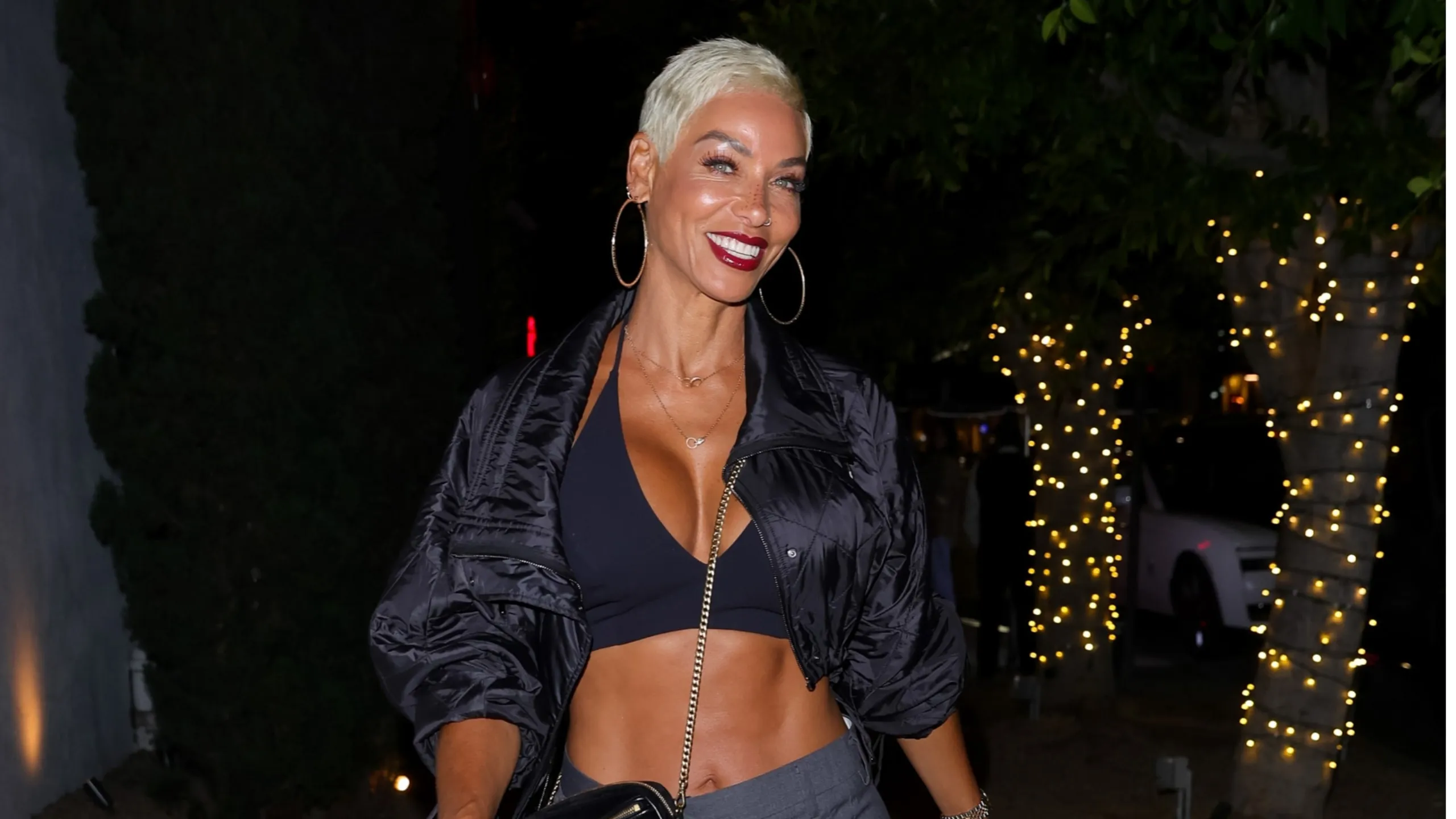 Wearing a black coat and pants, Nicole Murphy smiles for paparazzi outside of a steakhouse in LA